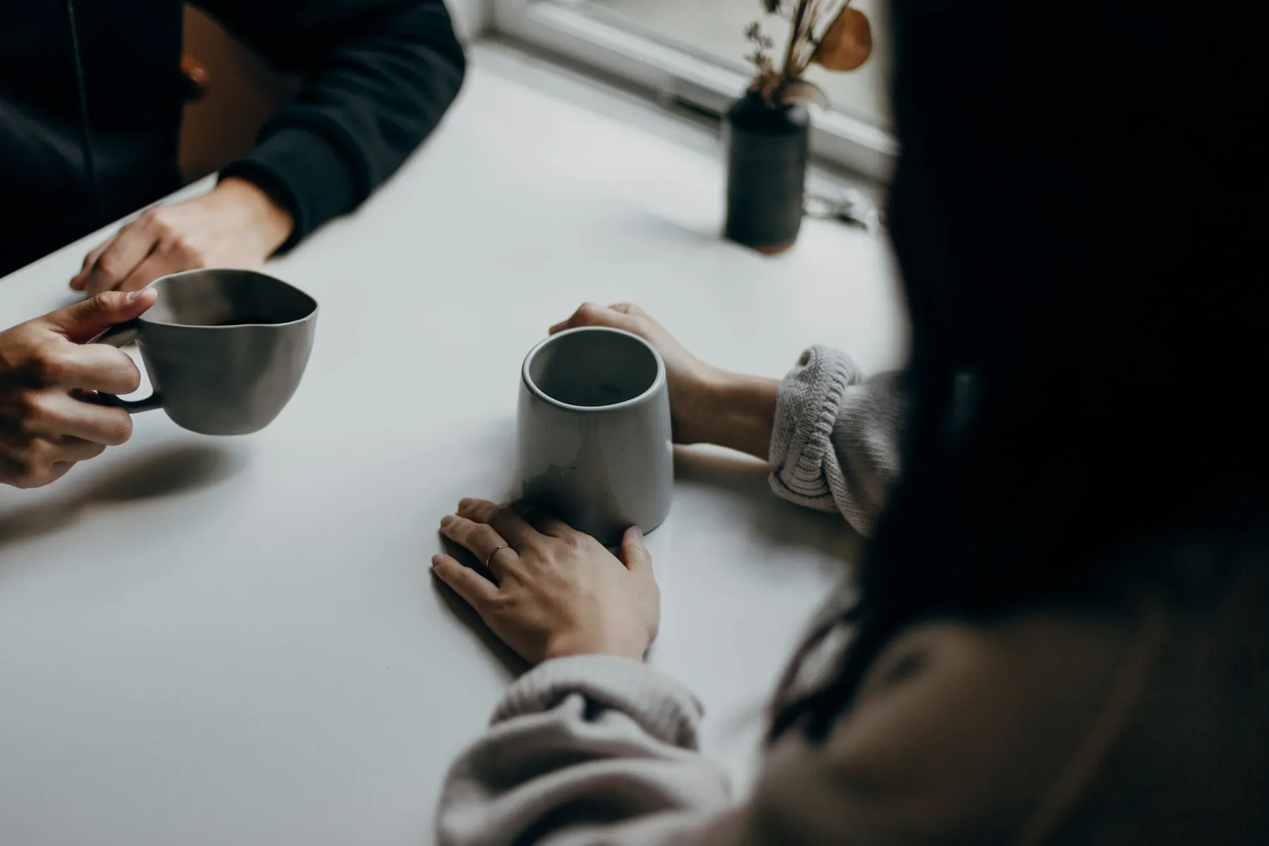Two people holding coffee mugs across a table.